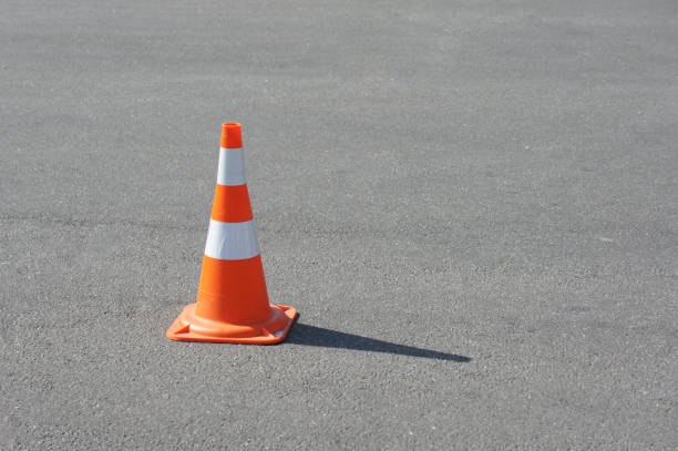 istock traffic cone, with white and orange stripes on gray asphalt, copy space. Bright weather 1418474470