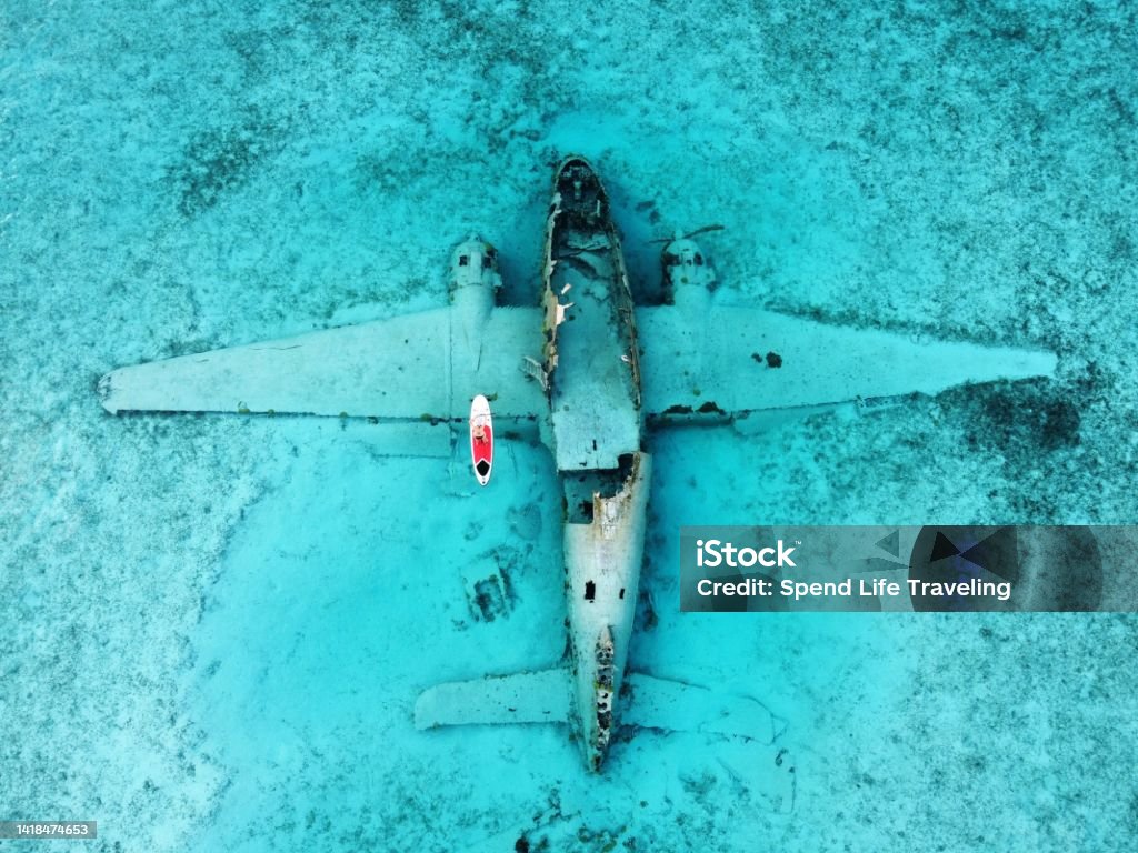 Paddleboarding Around A Plane Wreck in the Exumas, Bahamas A woman paddleboarding around the wreckage of a plane that landed in the water off of Norman's Cay in 1980.
This site is now a popular destination for snorkeling. Bahamas Stock Photo