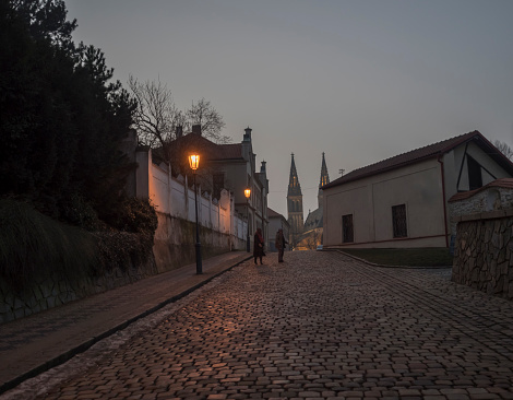 Czech Republic, Prague, February 23, 2021: Night view of Cobbled street at Vysehrad with lanterns and illuminated Basilica of St. Peter and Paul, gothic cathedral.