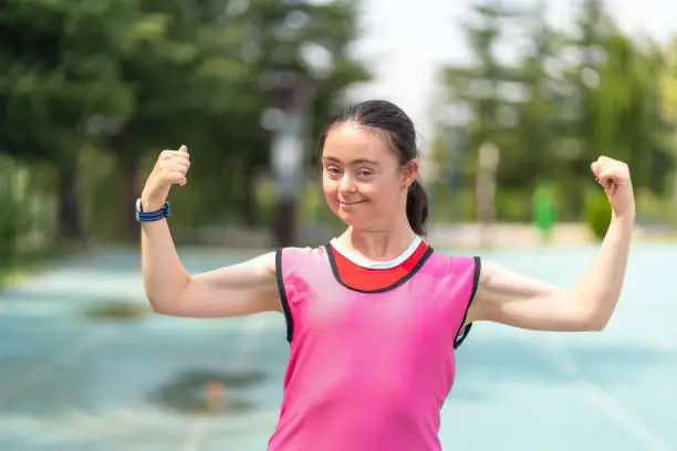 Young female athlete with Down syndrome posing at sport track and Flexing Muscles
