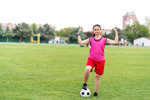 Portrait of Young female soccer player with Down syndrome posing at sport field and Flexing Muscles