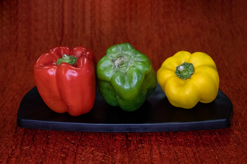 Green, red, yellow bell peppers on black platter. Dark background