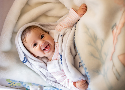 Beautiful baby girl smiling in her crib and looking very happy at the camera