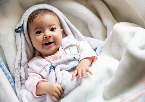 Portrait of a beautiful baby girl smiling in her crib and looking at the camera - childrens concepts