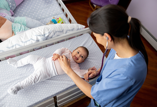 Latin American female doctor checking a baby girl  at home - pediatric medicine concepts