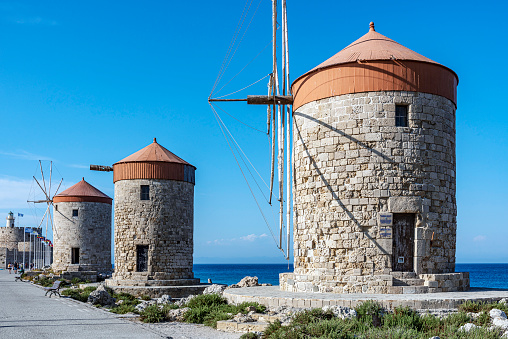 Three windmills and Saint Nicholas fortress at Mandraki Harbor in Rhodes, Greece