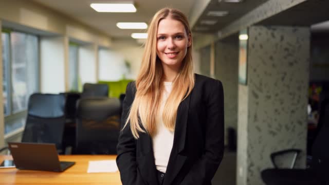 Smiling caucasian business woman in formal outfit looking at camera standing in office. Portrait of happy pretty businesswoman in jacket. Condfident female corporate worker posing indoors. Hero shot.