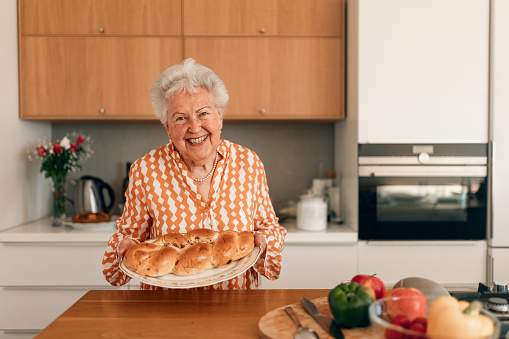 Happy senior woman holding homemade sweet braided bread with raisins.
