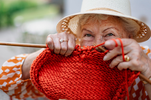 Portrait of senior woman sitting outdoor and knitting scarf.
