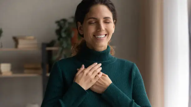 Photo of Sincere smiling young woman feeling grateful at home.