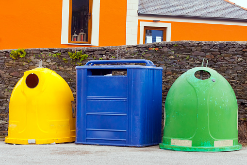 Multicolored garbage bins in a row by the sidewalk for recycling. Urban scene, stone wall,house. Navia, Asturias, Spain.