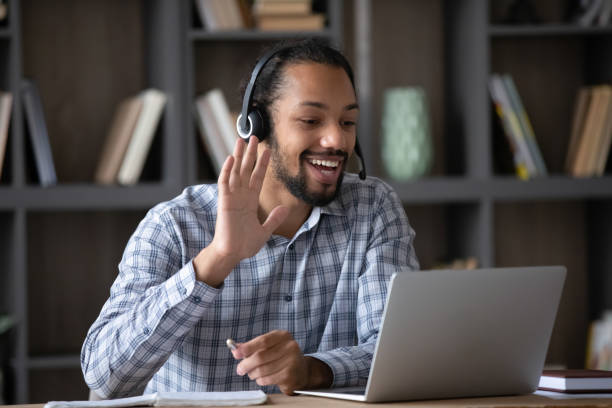 istock Cheerful happy Black student guy in headphones waving hand hello 1418517036