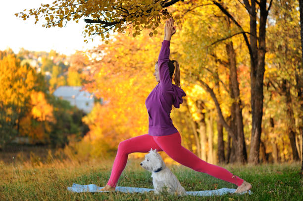 istock Woman practicing standing yoga pose with her dog in the forest 1418518907