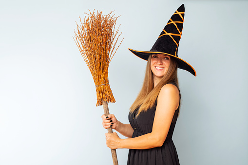 Happy Halloween! Happy young woman in halloween witch costume with broom on a light background. Halloween party concept.