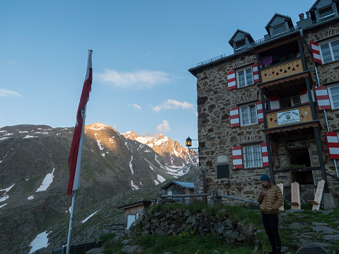 Stubai Valley, Innsbruck-Land, Tyrol, Austria, July 4, 2020: young hiker woman standing in front of Nuernberger Huette, an alpine mountian hut at su.nny summer evening, golden hour light