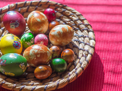 Czech republic, Prague, April 4, 2018: Homemade Colorful Painted easter eggs in straw flat basket with easter stickers on red tablecloth background, selective focus. Top view, horizontal.