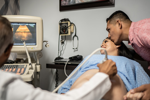 Obstetrician using ultrasound scanner on pregnant mid adult woman in his office at the hospital