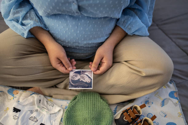 Pregnant woman looking at ultrasound results in the bed at home Pregnant woman looking at ultrasound results in the bed at home surrogacy stock pictures, royalty-free photos & images