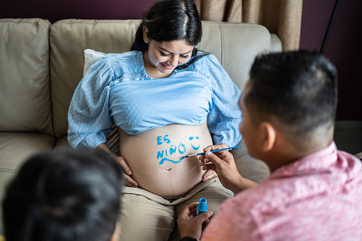 Family painting mother's pregnant belly in the living room at home