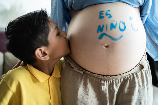 Son kissing pregnant mother belly and doing gender reveal at the living room