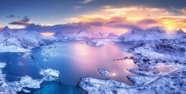 vista aérea do mar azul, ilhas de neve, montanhas, céu com nuvens rosas ao pôr do sol no inverno. ilhas lofoten, noruega. paisagem com pedras na neve, reflexo na água. vista superior do drone. natureza - lofoten and vesteral islands - fotografias e filmes do acervo