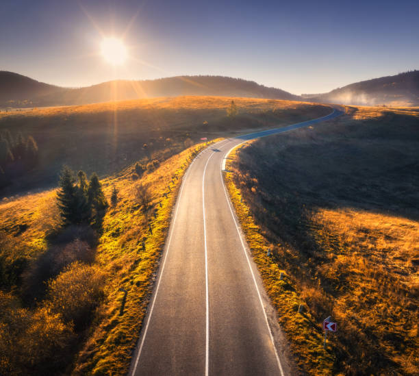 luftaufnahme der bergstraße bei sonnenuntergang im herbst in der ukraine. drohne der straße im wald. schöne landschaft mit fahrbahn in hügeln, pinien, wiesen, goldenem sonnenlicht im herbst. reise - ansicht von oben stock-fotos und bilder