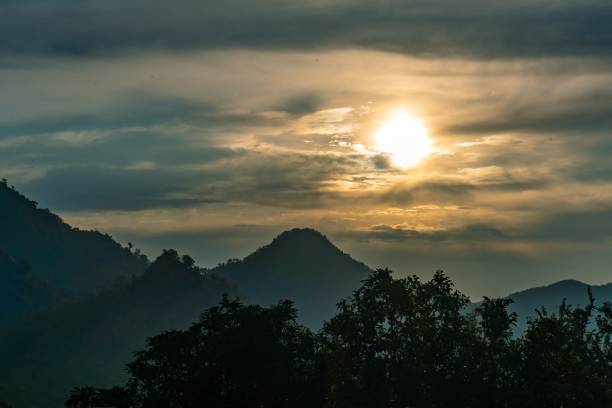 istock Silhouette of mountains with the Sun shining through clouds during sunset 1418531937