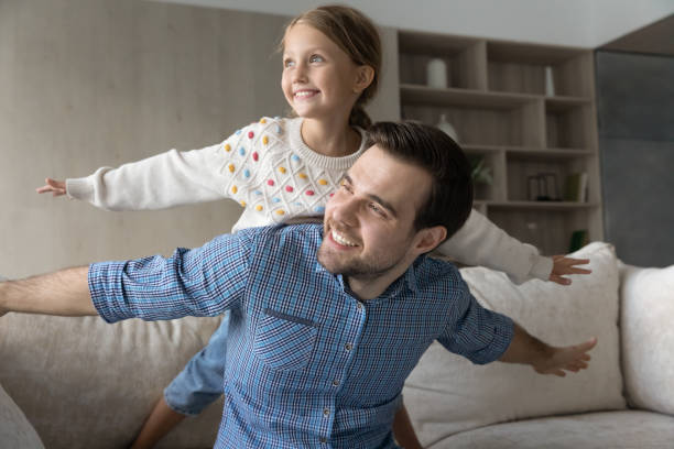 istock Cheerful daddy and happy daughter kid playing airplane on couch 1418536385