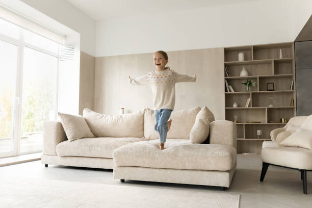 istock Excited cheerful girl kid jumping on comfortable couch 1418536534
