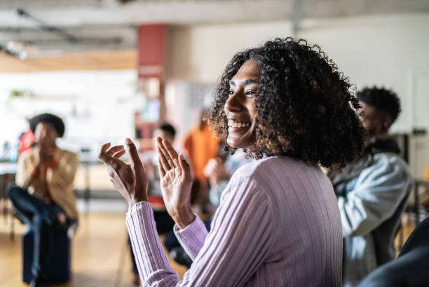 Young woman clapping in a seminar or group therapy Young woman clapping in a seminar at a coworking lecture hall training classroom presentation stock pictures, royalty-free photos & images