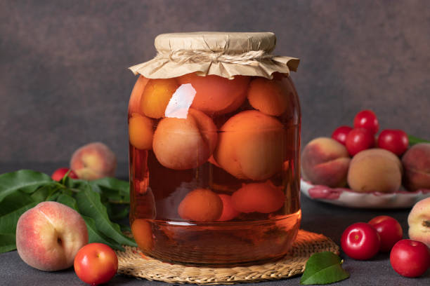 Homemade compote with peaches and cherry plum in glass jar on brown background, front view stock photo