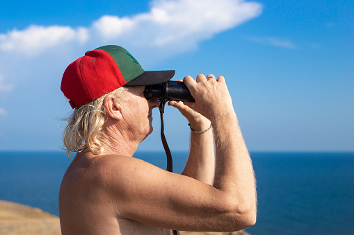 Adult A man with binoculars looks at the sea in the distance, on a summer sunny day. close-up.