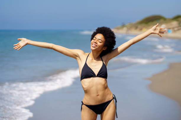 istock Cheerful black woman in bikini on wet seashore 1418556328