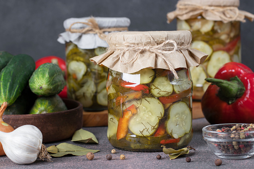 Pickled cucumbers salad with sweet peppers and onions in jars on dark gray table
