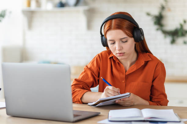istock Distance learning, online education. Concentrated young female student using laptop for studying remotely at home, watching the training, listening to the webinar 1418560331