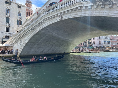 dolier transporting tourists under the Rialto Bridge on a bright sunny day in Venice, Italy