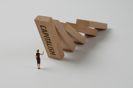 Businesswoman figurine trying to stop the domino effect. Capitalism concept.