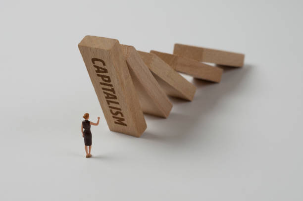Dominos: Capitalism Businesswoman figurine trying to stop the domino effect. Capitalism concept. capitalism stock pictures, royalty-free photos & images
