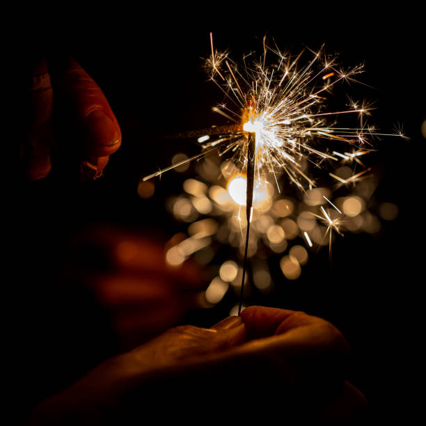 um brilho aceso queimando, com um fundo preto - sparkler sparks new years eve human hand - fotografias e filmes do acervo