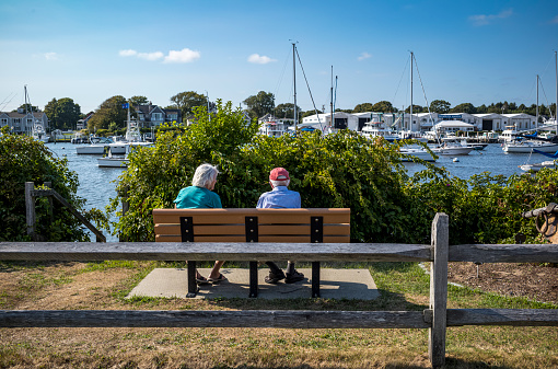 An elderly couple relaxing on a bench overlooking Falmouth Harbour in Falmouth, MA on Cape Cod.