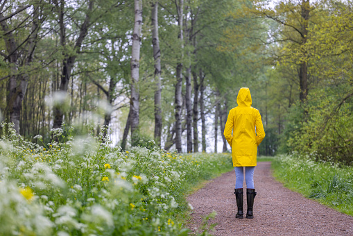 Young woman with yellow raincoat and rubber boots in spring nature