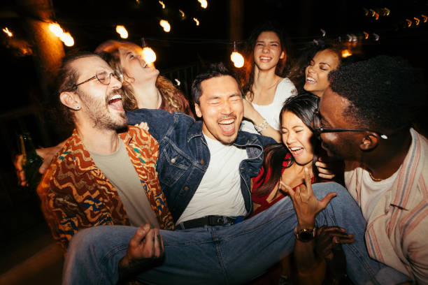 los amigos levantan a su amigo masculino en la fiesta nocturna al aire libre en la azotea. - hombre de fiesta fotografías e imágenes de stock