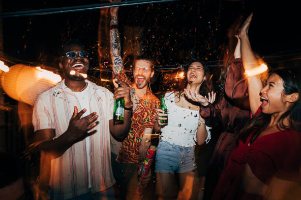 un groupe d’amis célèbre avec des confettis lors d’une fête nocturne sur le toit. - fête photos et images de collection