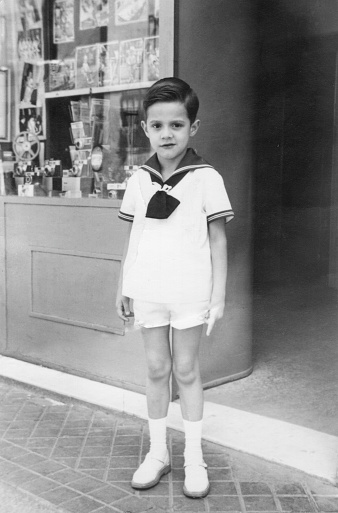 Black and White Vintage image taken in the 60s, little boy looking at the camera full length dressing with a sailor outfit, 1960