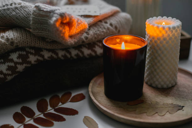 Two burning candles and stack of warm cozy sweaters on bedtable. Cozy autumn evening at home Two burning candles and stack of warm cozy sweaters om bedtable. Cozy autumn evening at home. Selective focus hygge stock pictures, royalty-free photos & images