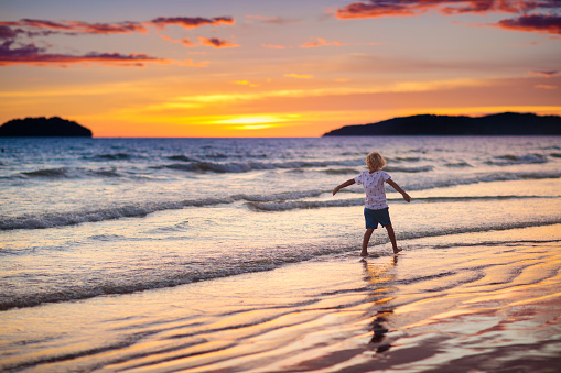 Child playing on ocean beach. Kid jumping in the waves at sunset. Sea vacation for family with kids. Little boy running on tropical beach of exotic island during summer holiday.