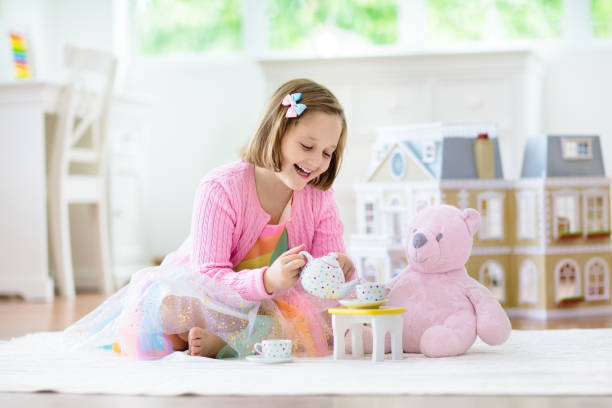Little girl playing with doll house. Kid with toys Little girl playing with doll house in white sunny bedroom. Kid with toys. Role game for young children. Child with teddy bear toy. Kids play tea party with stuffed animals and dolls. Nursery interior girl playing with doll stock pictures, royalty-free photos & images