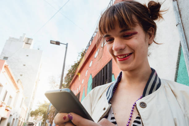 beautiful young latin transgender woman outdoors laughing and checking phone stock photo
