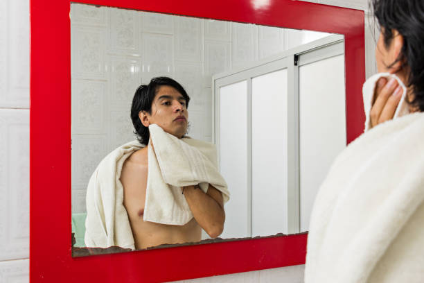 istock young man drying his face with a towel while looking at himself through a mirror 1418614342