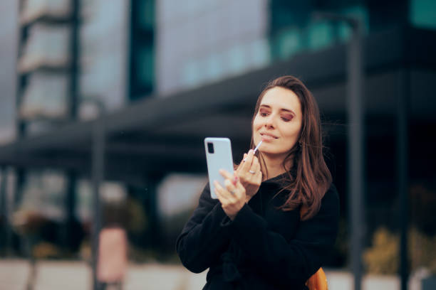 istock Woman Using Smartphone to Check her Lip Gloss Application 1418621047